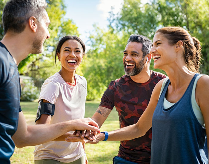 Group of active mature friends in park stacking hands after workout